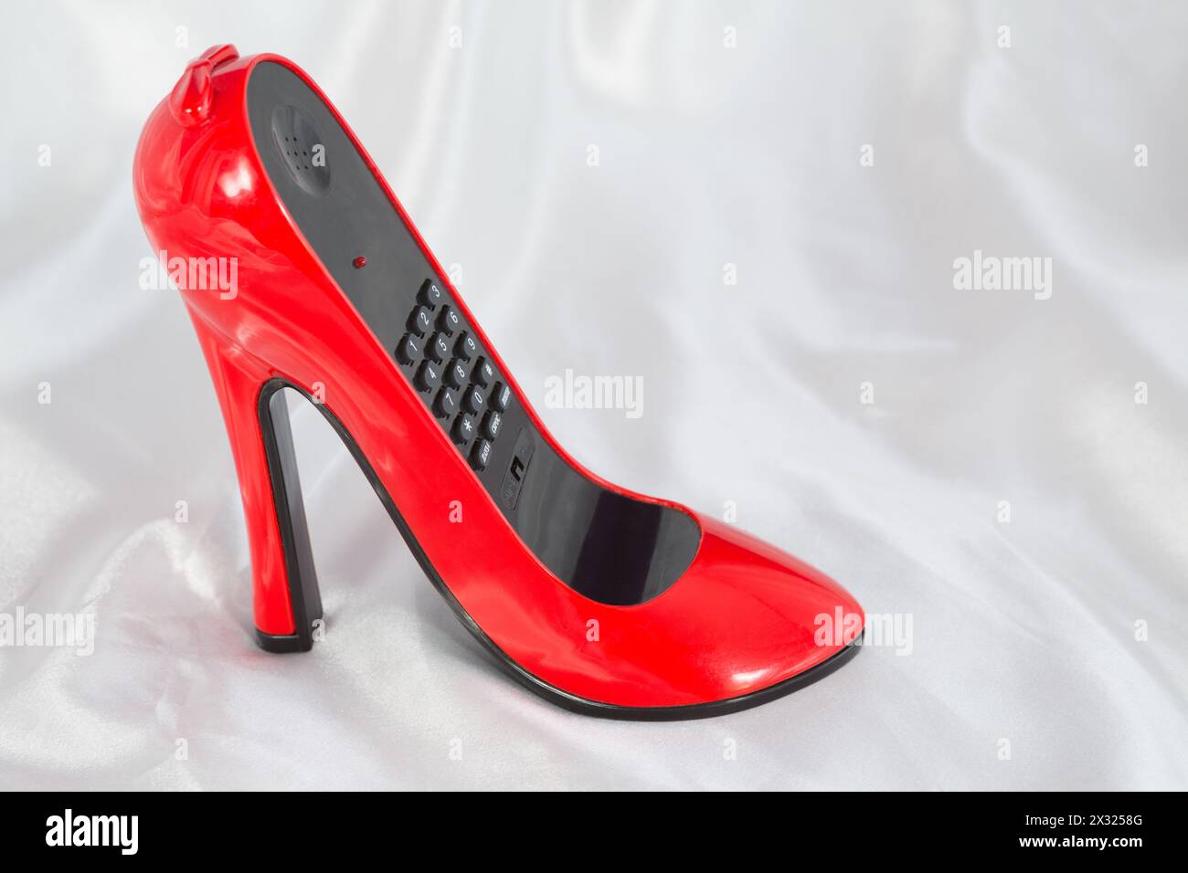 The stylish phone in the form of red female high-heeled shoes on the satin cloth Stock Photo