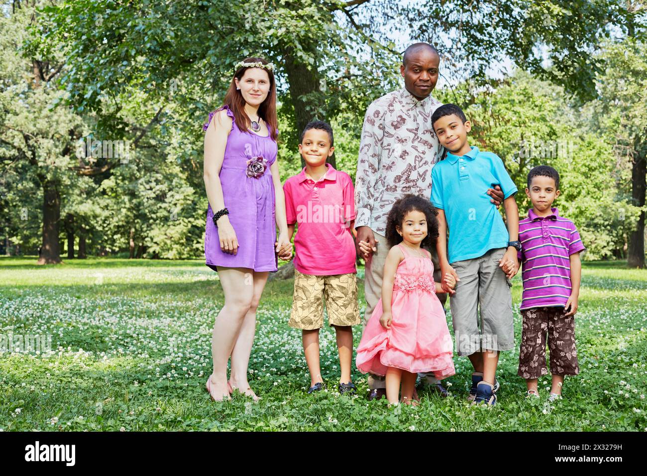 Mixed race family of six stands holding hands in park on summer day Stock Photo