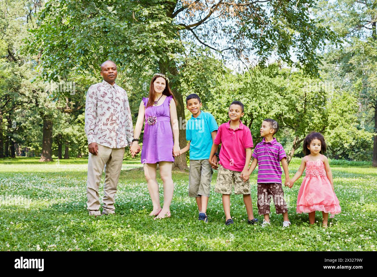 Mixed race family of six stands according to height and holding hands in park Stock Photo