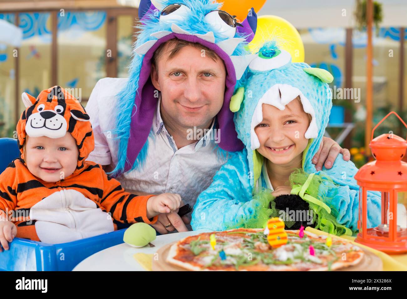 Father with daughter in monster costumes and baby boy in tiger costume celebrate the birthday in a cafe Stock Photo