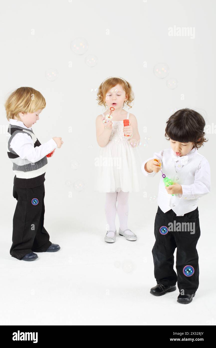 Little happy girl and two boys blow bubbles on white background. Stock Photo