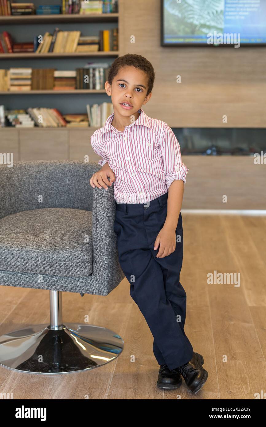Little boy in shirt standing in the business center of leaning on the chair Stock Photo
