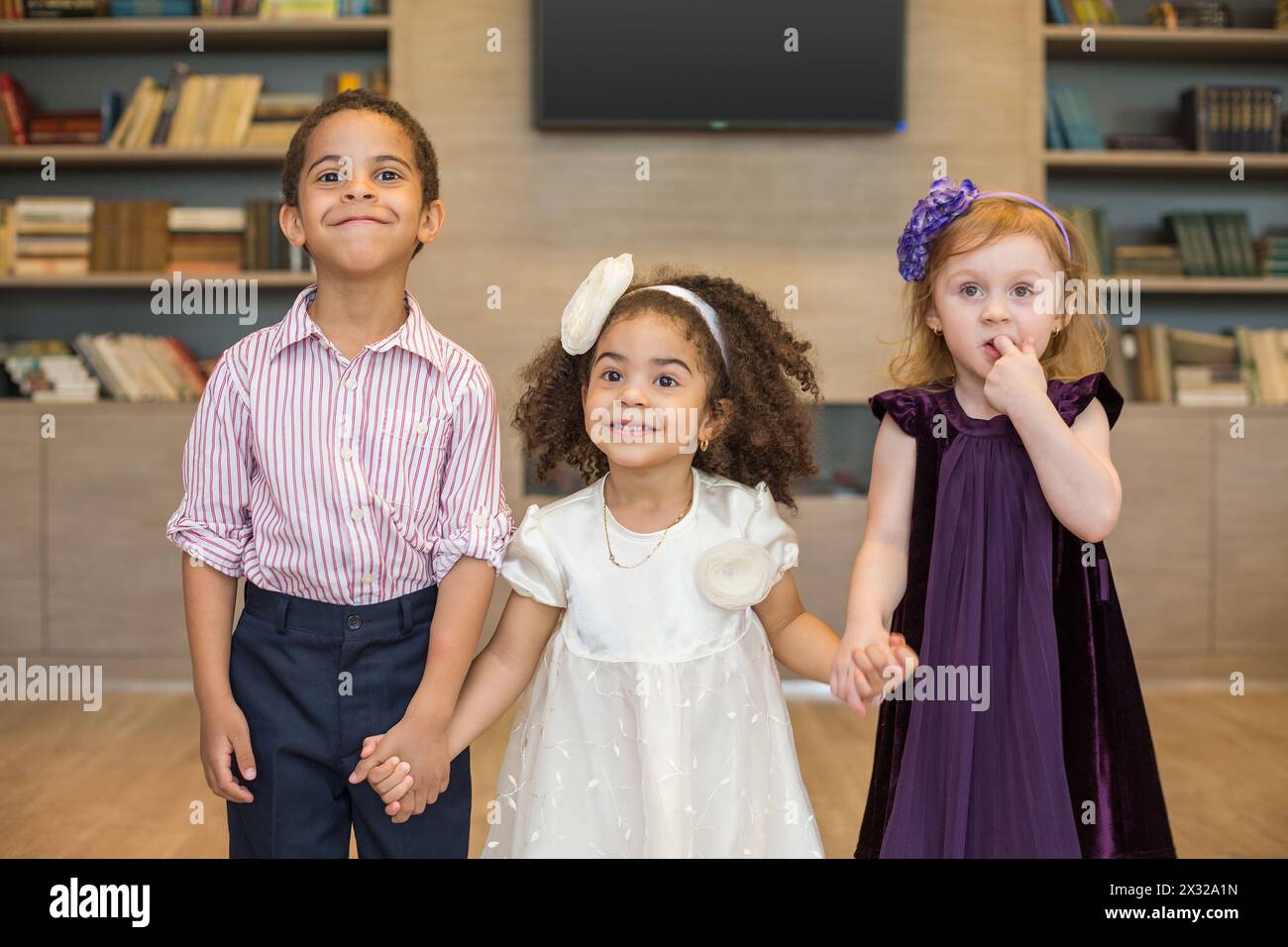 Three little children in celebratory clothes holding hands in a business center Stock Photo
