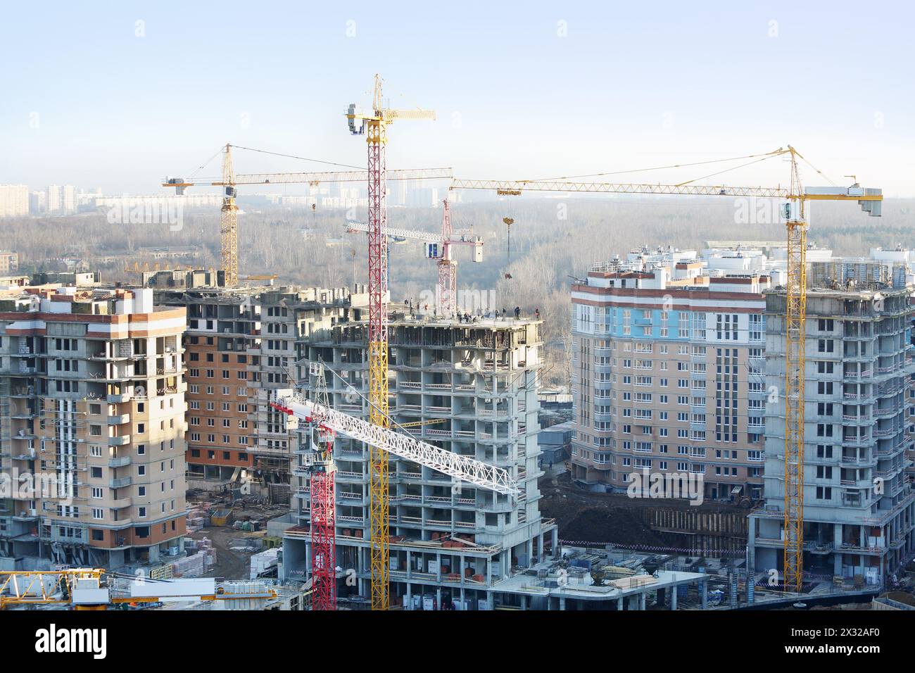 Many residential multi-storey buildings under construction and yellow cranes at sunny day. Stock Photo