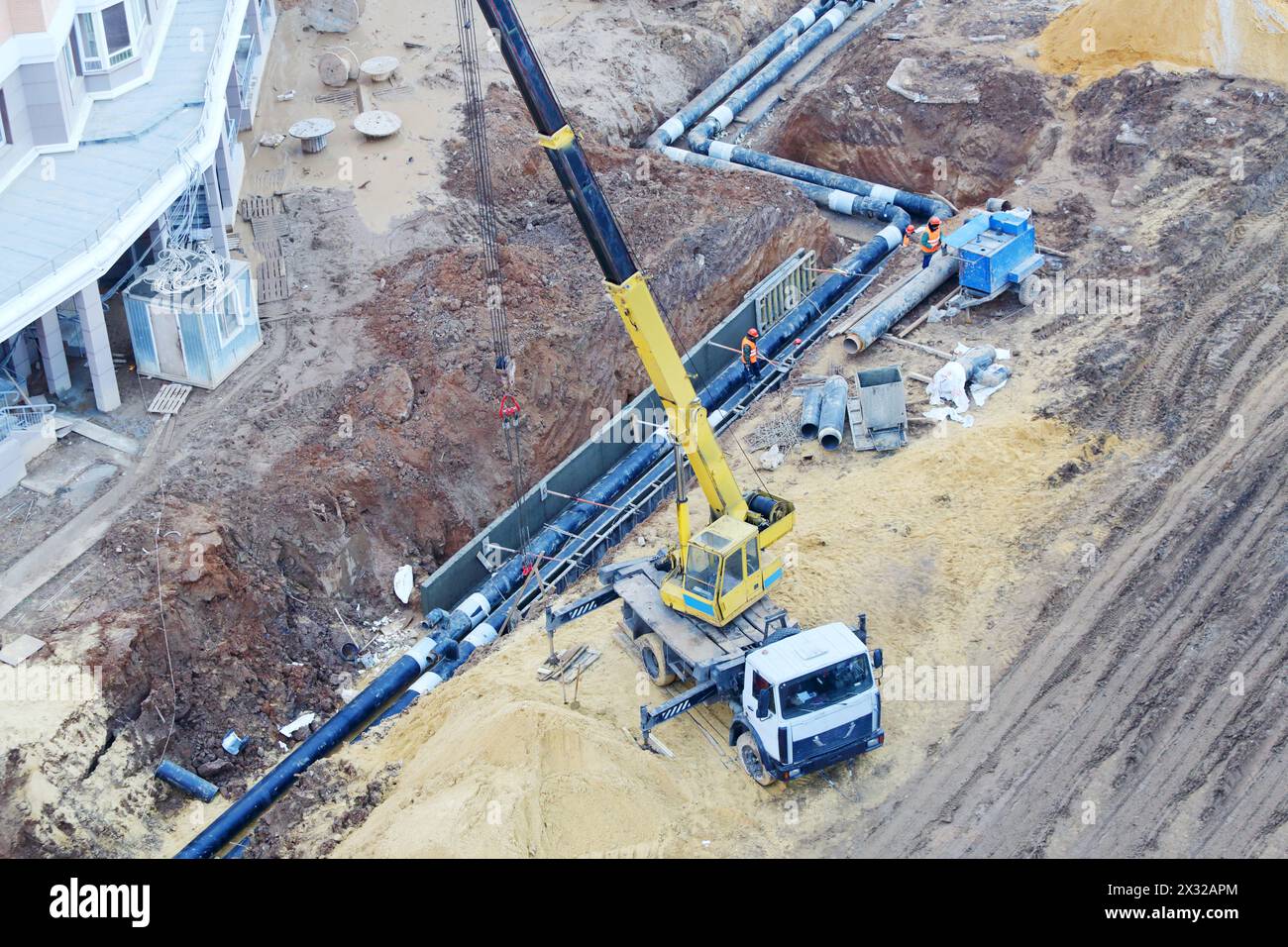 Truck Crane puts underground pipes at large construction site. Stock Photo
