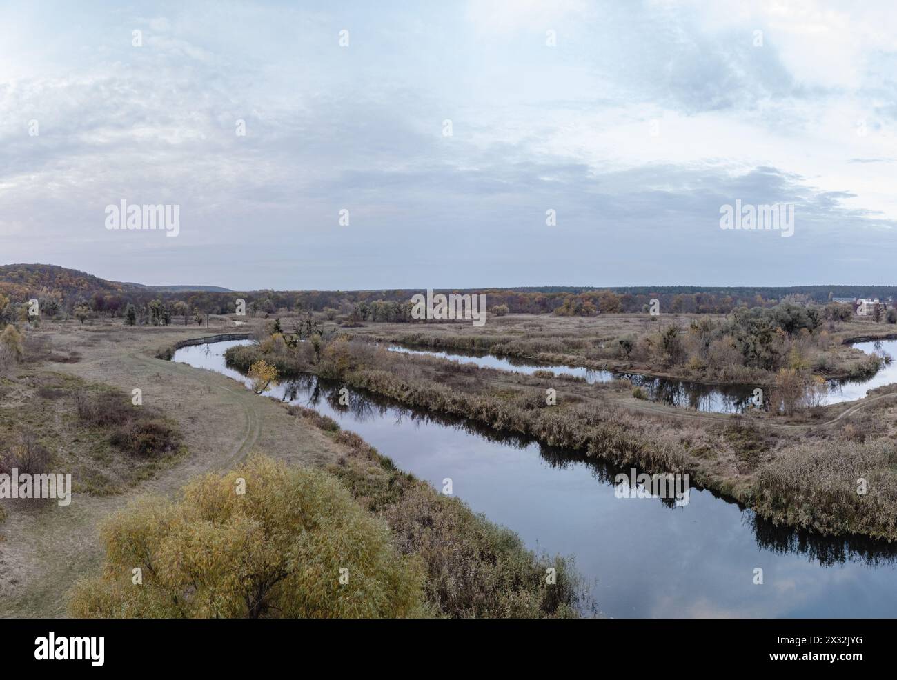 Aerial dirt road on Siverskyi Donets river coast with autumn forest and cloudy sky in Ukraine Stock Photo