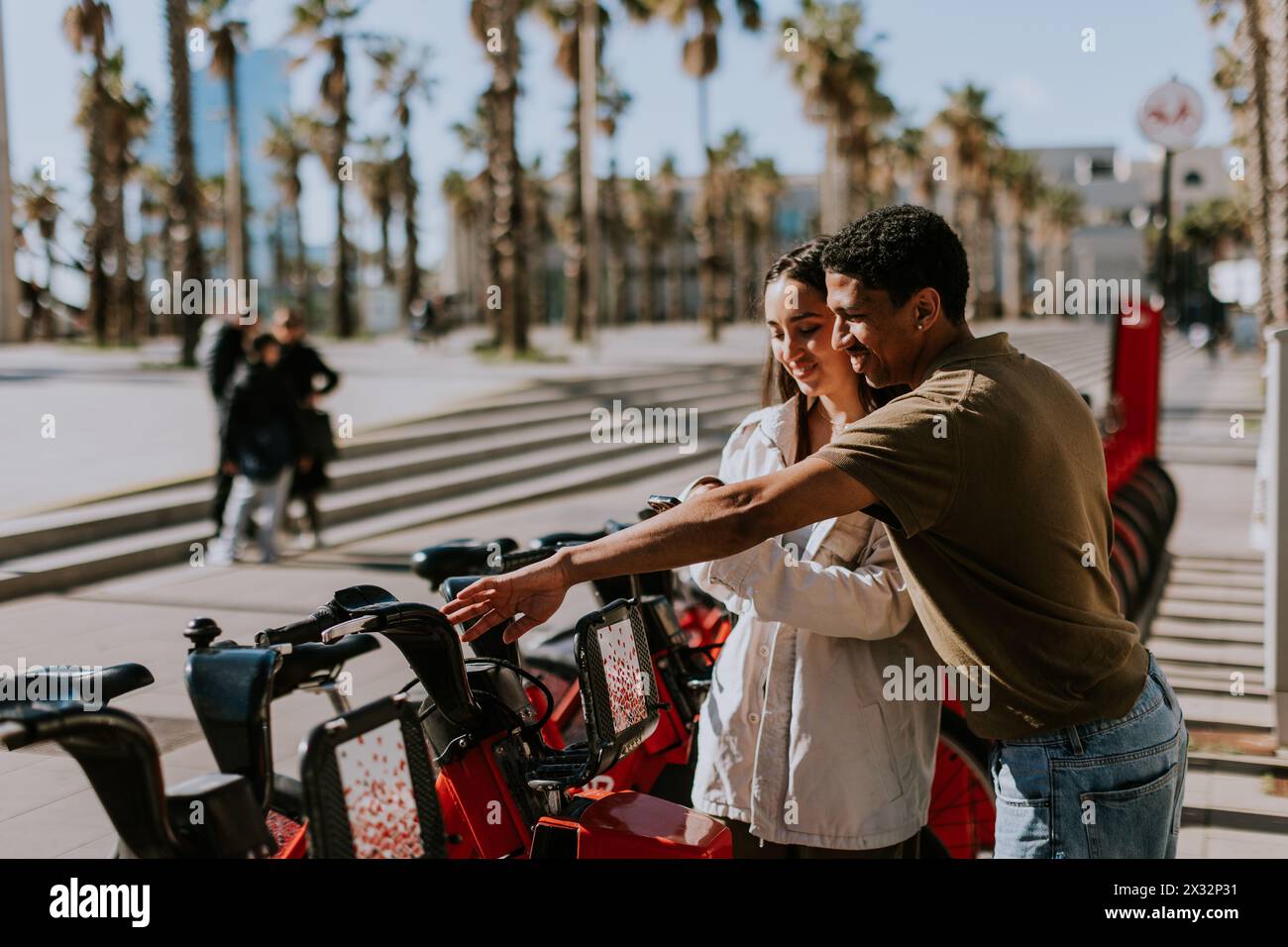 Young pair enjoying a breezy day choosing bikes from a rental station in Barcelona. Stock Photo