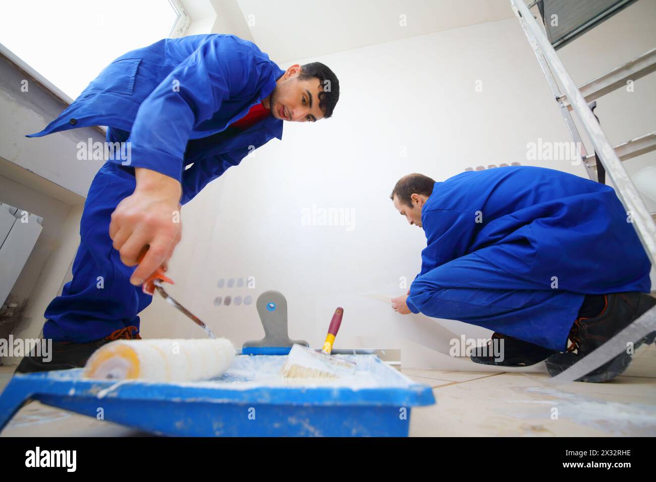 Workers in blue glue paint fiberglass and paint walls in new apartment Stock Photo