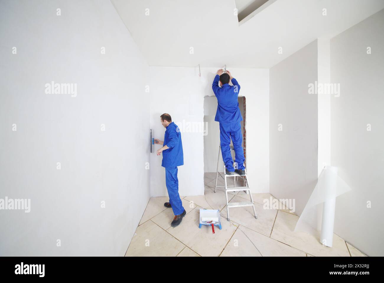 Skillful workers in blue glue paint fiberglass on ladder in new apartment Stock Photo