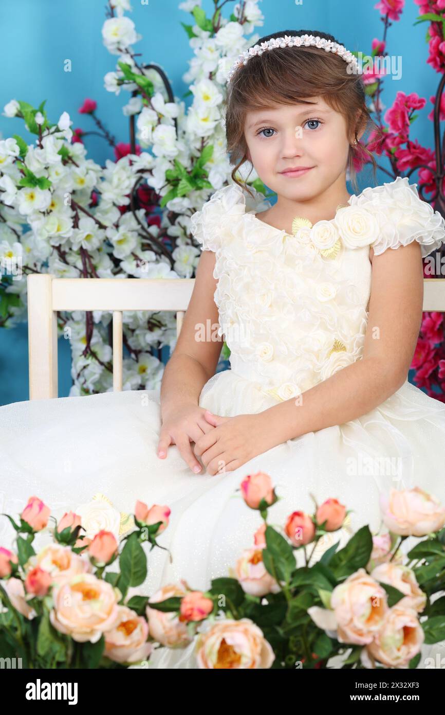 Cute little girl in white dress sits on bench among flowers Stock Photo ...