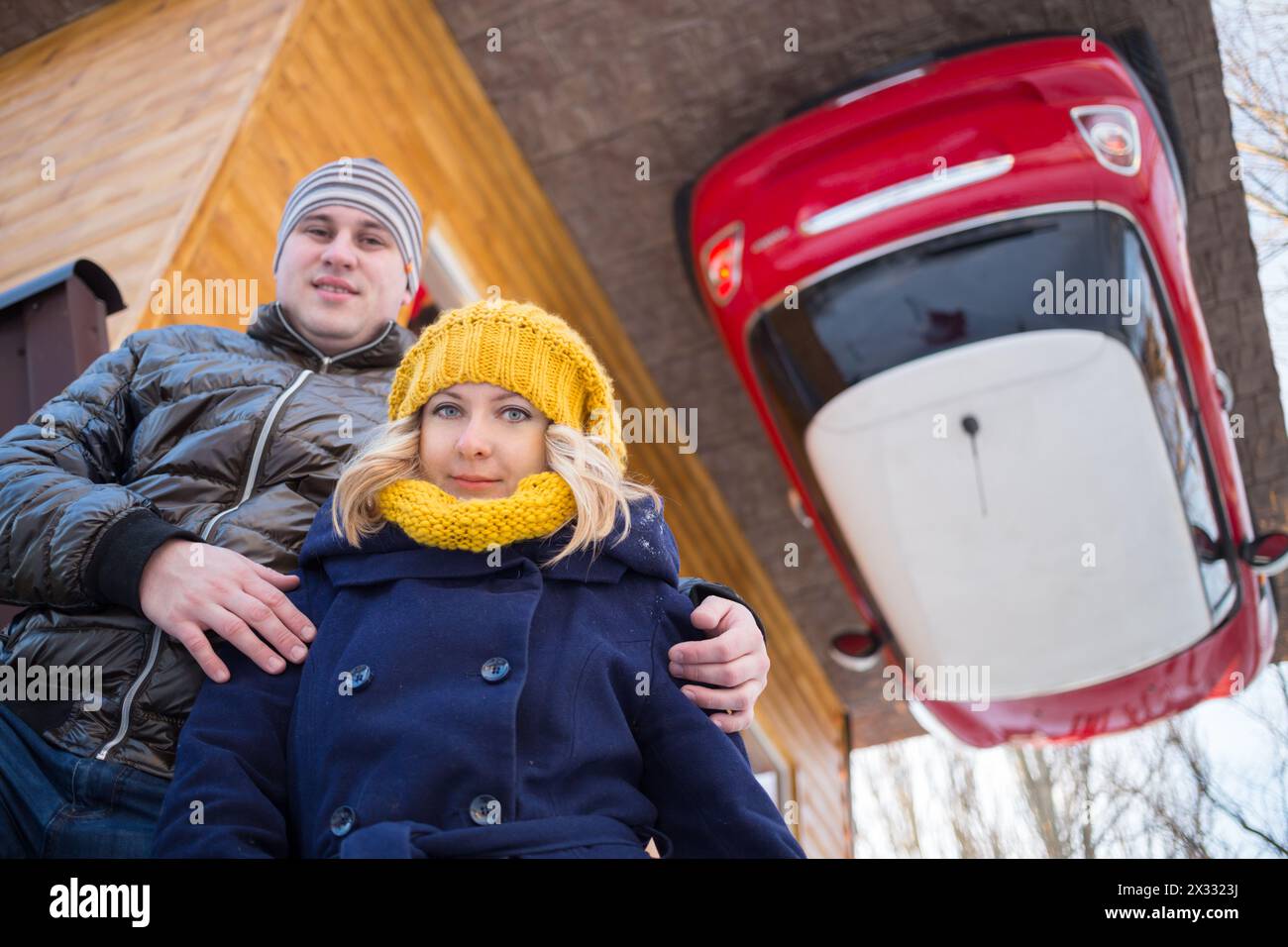 Couple against the inverted house with red car Stock Photo