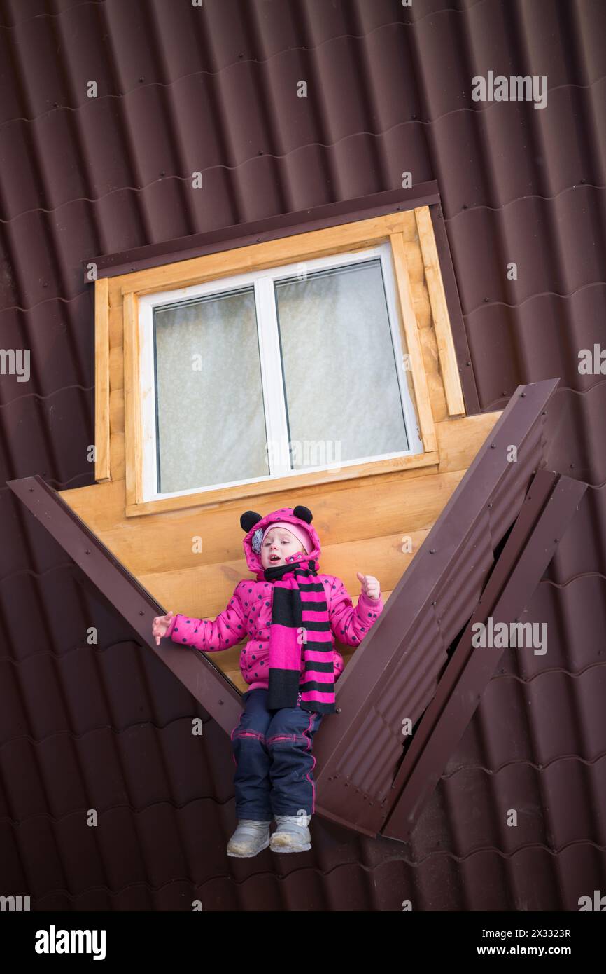 Little girl sitting on the brown roof of the upside-down house Stock Photo