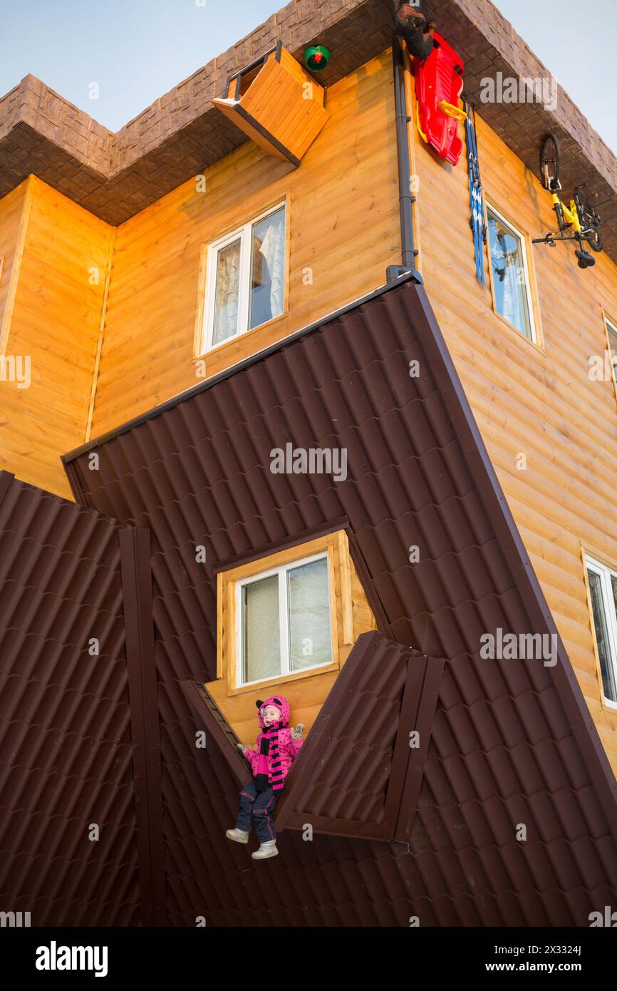 Little girl sitting on the roof of the upside-down house Stock Photo
