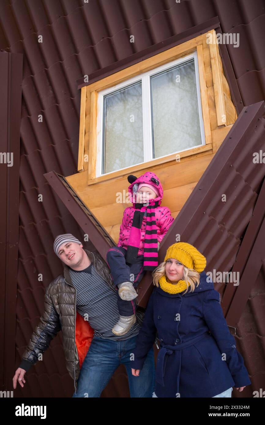 Family of three against the roof of real inverted house Stock Photo