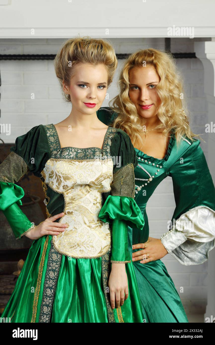 Two beautiful women in green medieval costumes stand near chimney with ...