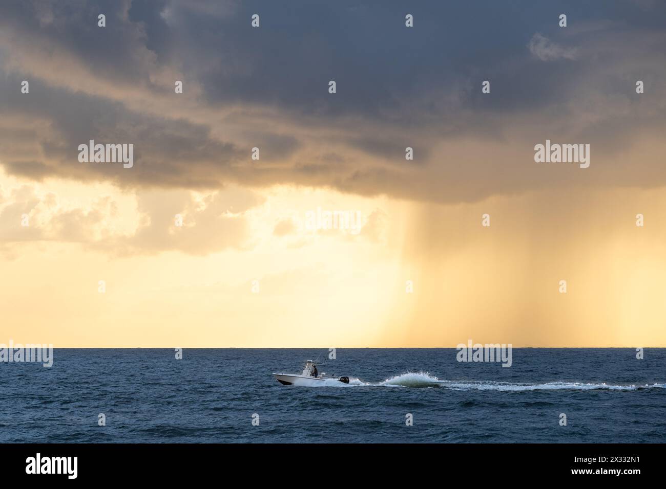 A fishing boat cruises along the shoreline at sunrise in South Ponte Vedra Beach as an approaching cloud drops a column of rain over the ocean. (USA) Stock Photo