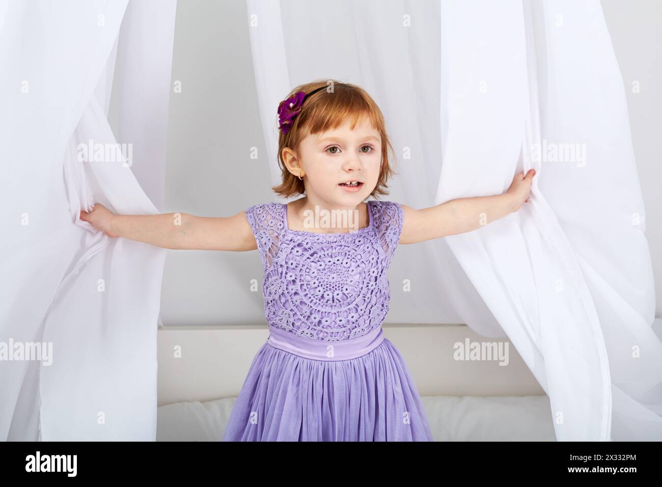 Little girl dressed in holiday clothes looks out from under tent over bed Stock Photo