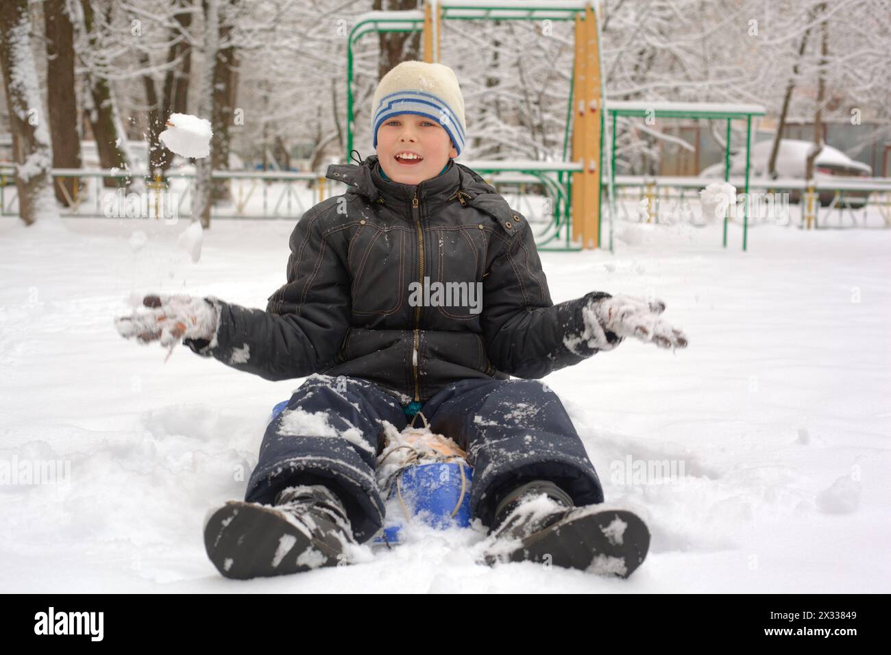 laughing boy sits in a snowdrift and plays snowballs Stock Photo