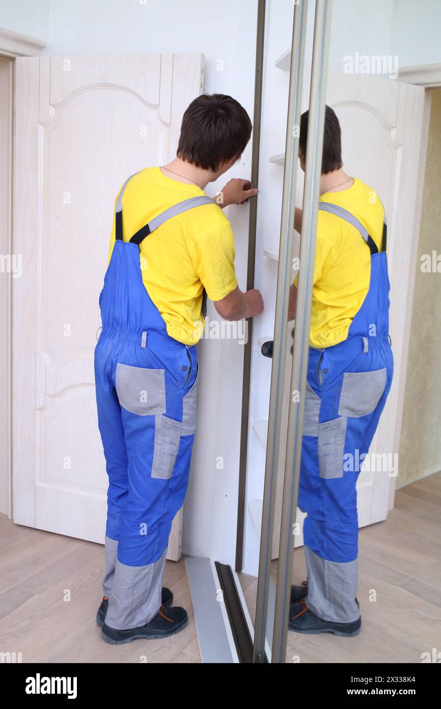 Worker fixing mirrored doors on corner sliding wardrobe in room Stock