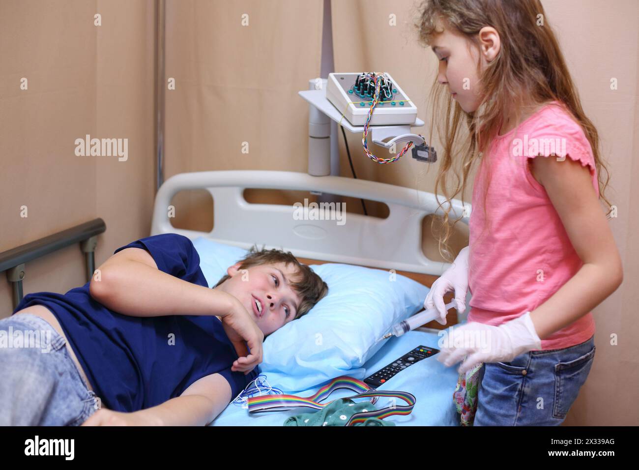 Girl standing with a syringe in hand near the boy lying on the bed in a hospital ward Stock Photo