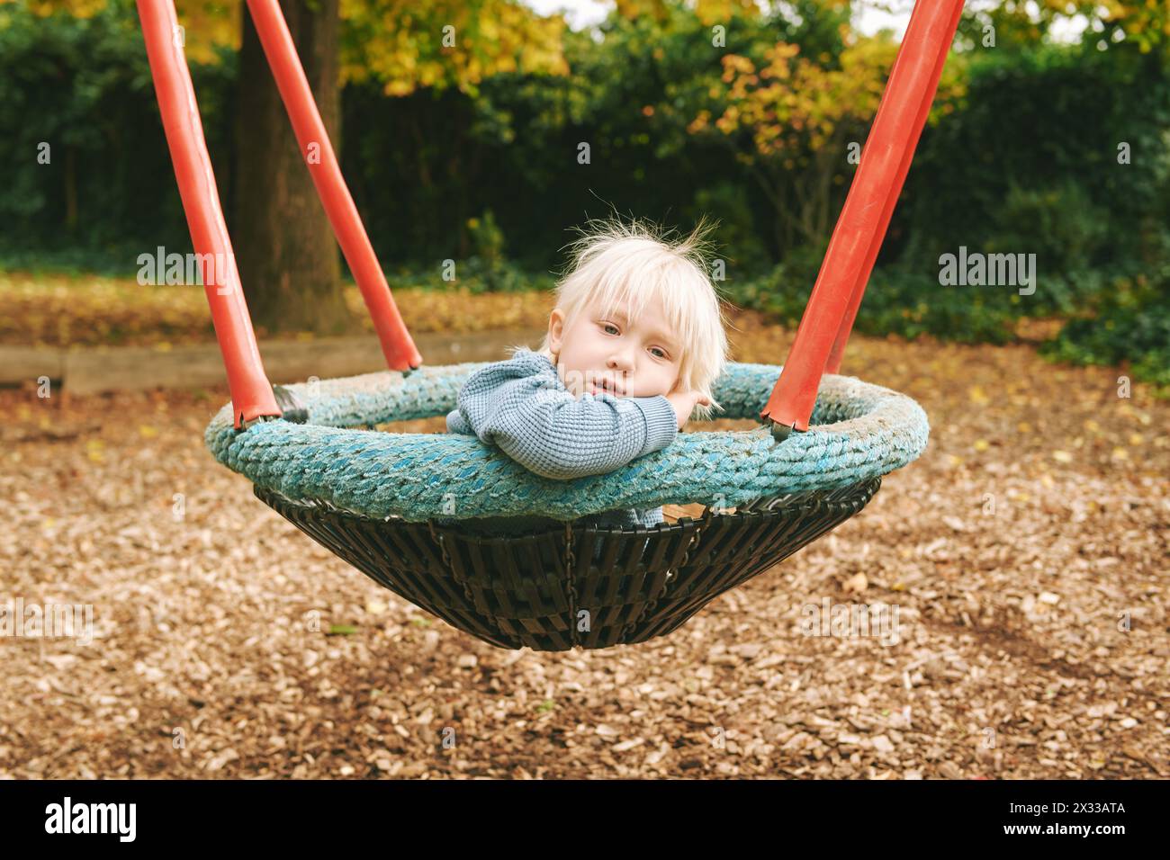 Outdoor portrait of adorable little sad boy relaxing on swing on playground Stock Photo