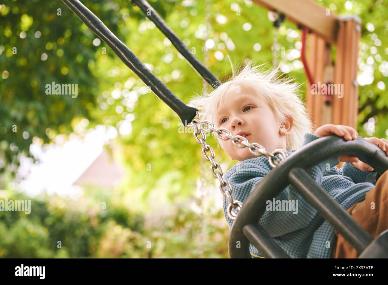 Outdoor portrait of adorable little boy having fun on swing on playground Stock Photo