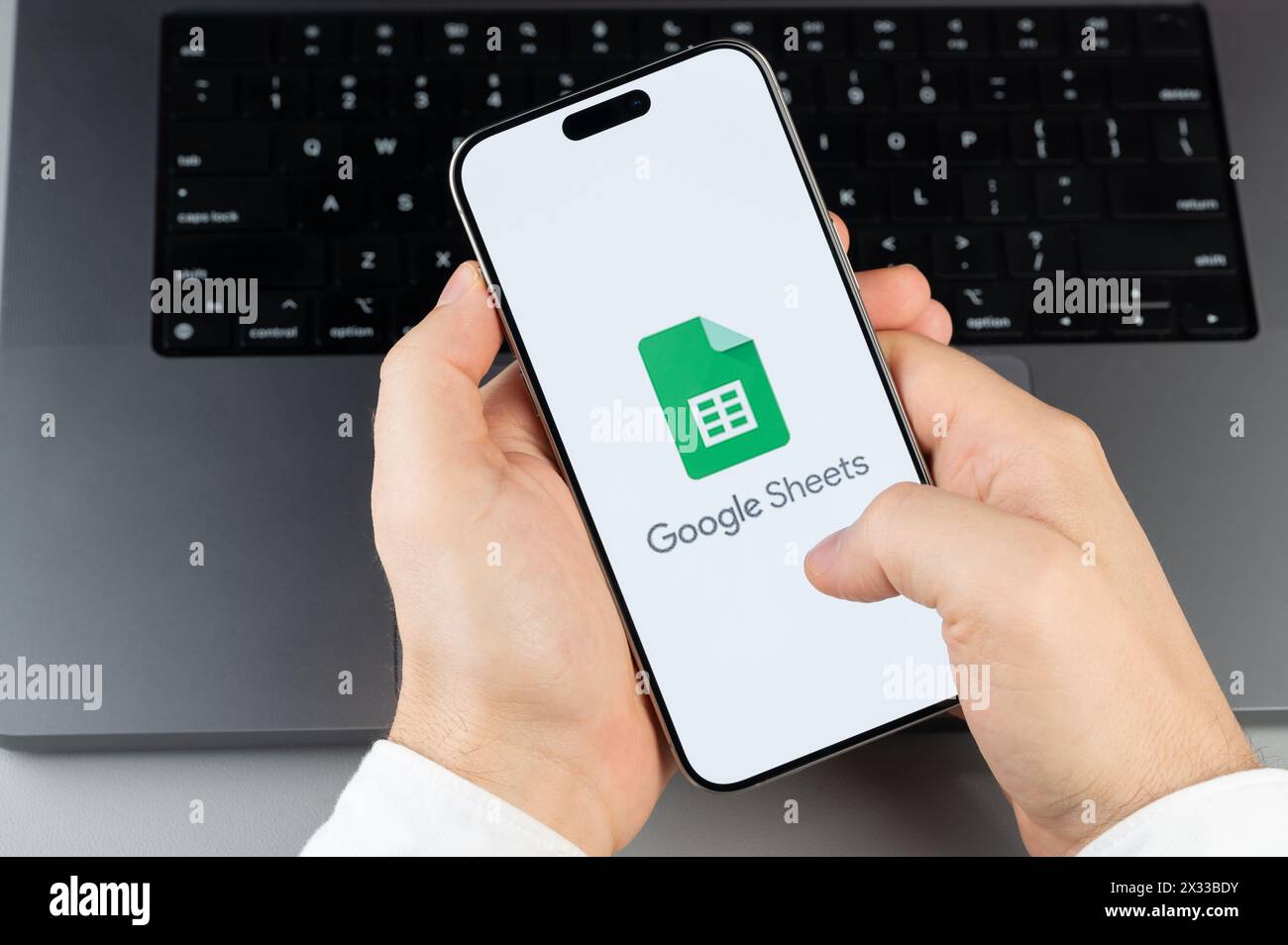 New York, USA - April 6, 2024: Popular Google sheets  mobile app on smartphone screen in hands on laptop keyboard background Stock Photo