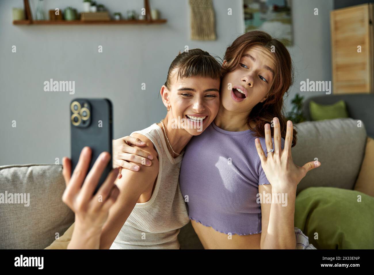 Beautiful lesbian couple in comfy attire sitting closely on a couch. Stock Photo