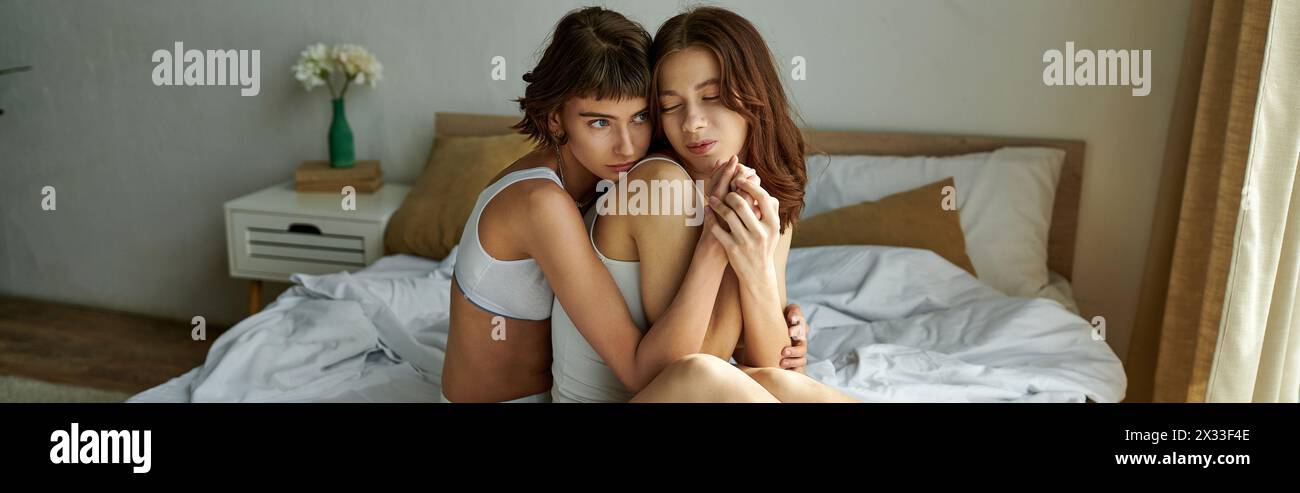 Intimate moment with two women in casual attire sitting on bed. Stock Photo