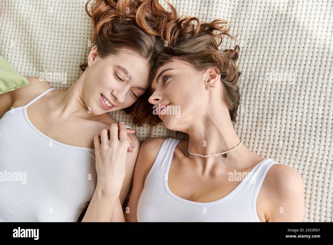 Two women in comfy attire lying next to each other on a bed. Stock Photo
