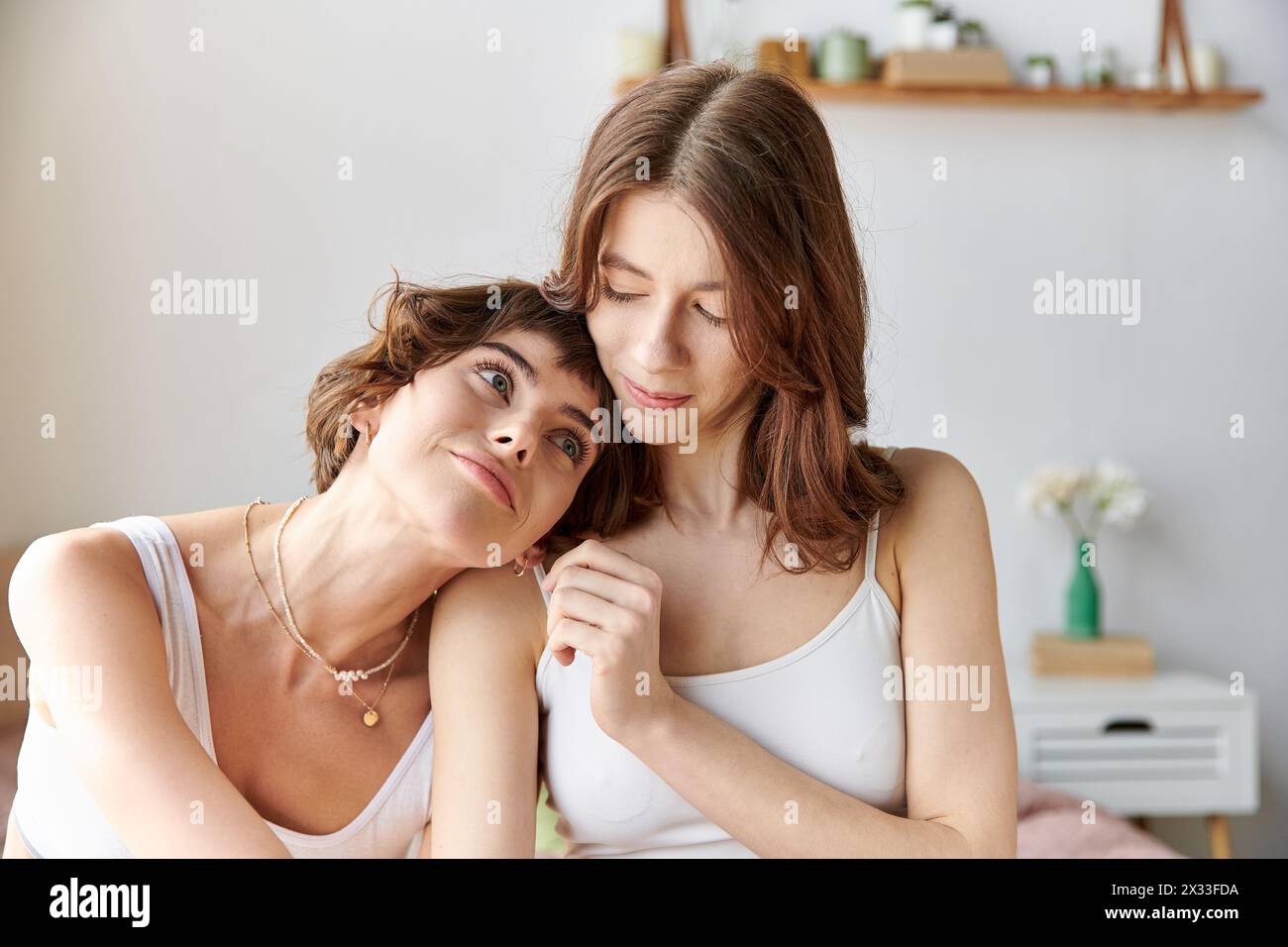 Two women in comfy attire sitting next to each other on a bed. Stock Photo