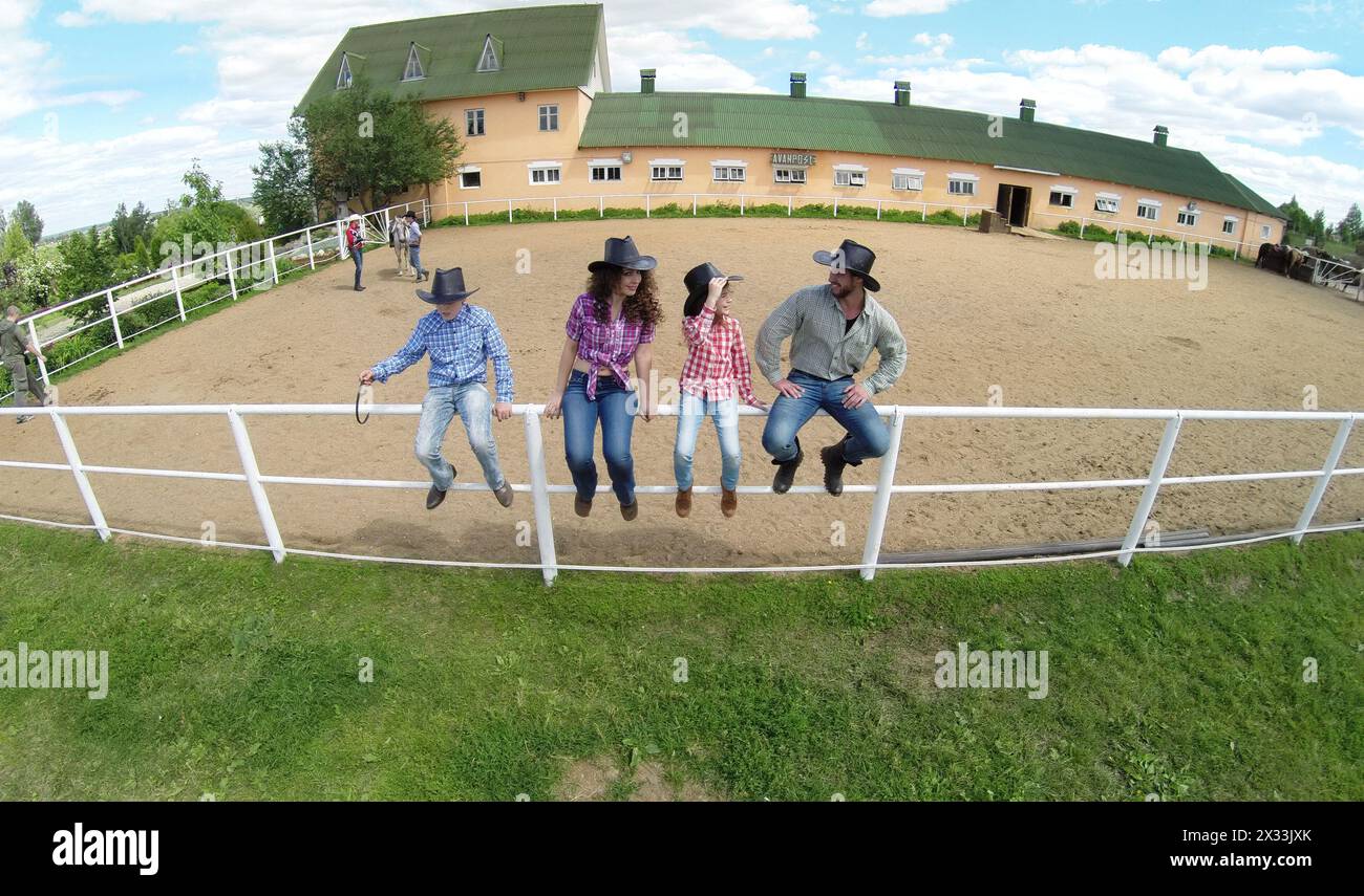 Four members family sit on fence near stable of ranch at summer sunny