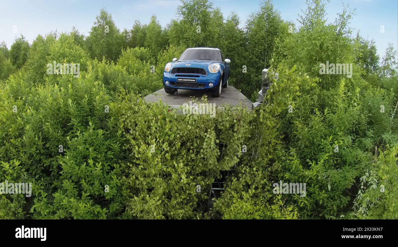 RUSSIA, NICOLA-LENIVETS - JUL 5, 2014: Mini cooper among leaves on trees near field with people in Wonderland Park during 9th International Festival o Stock Photo
