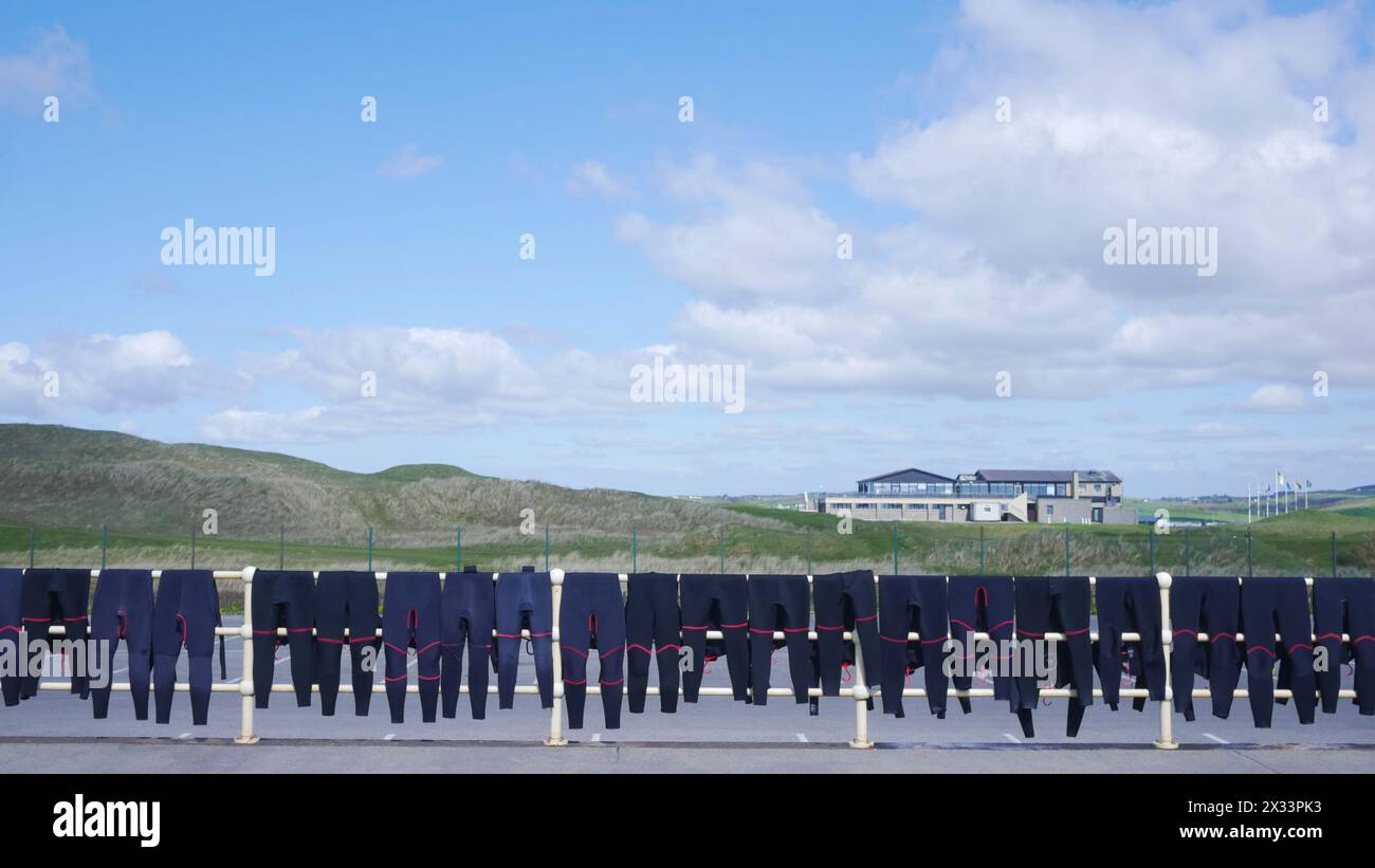 School's out for summer. Wet suits drying on a fence at the local surf school with Lahinch golf course in the background. Stock Photo