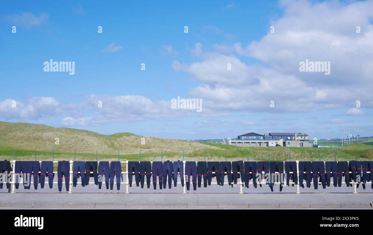 School's out for summer. Wet suits drying on a fence at the local surf school with Lahinch golf course in the background. Stock Photo