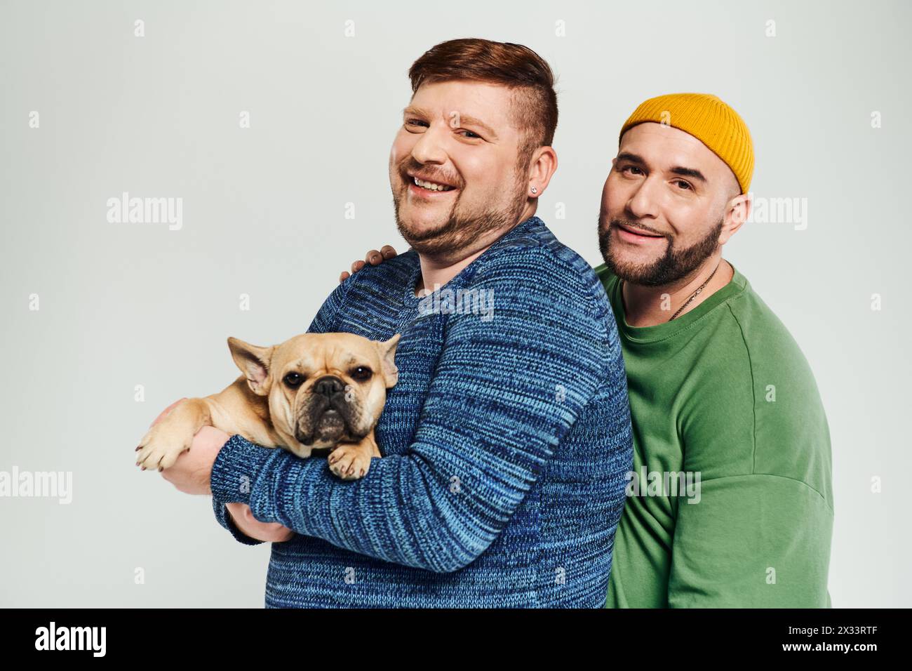 Two men lovingly hold a small dog in their arms, enjoying time together. Stock Photo