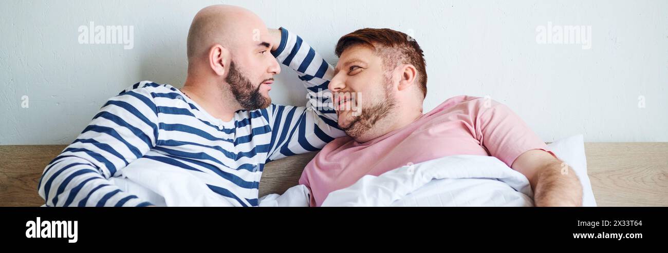 Two men cuddle on a cozy bed, bonded by love and warmth. Stock Photo