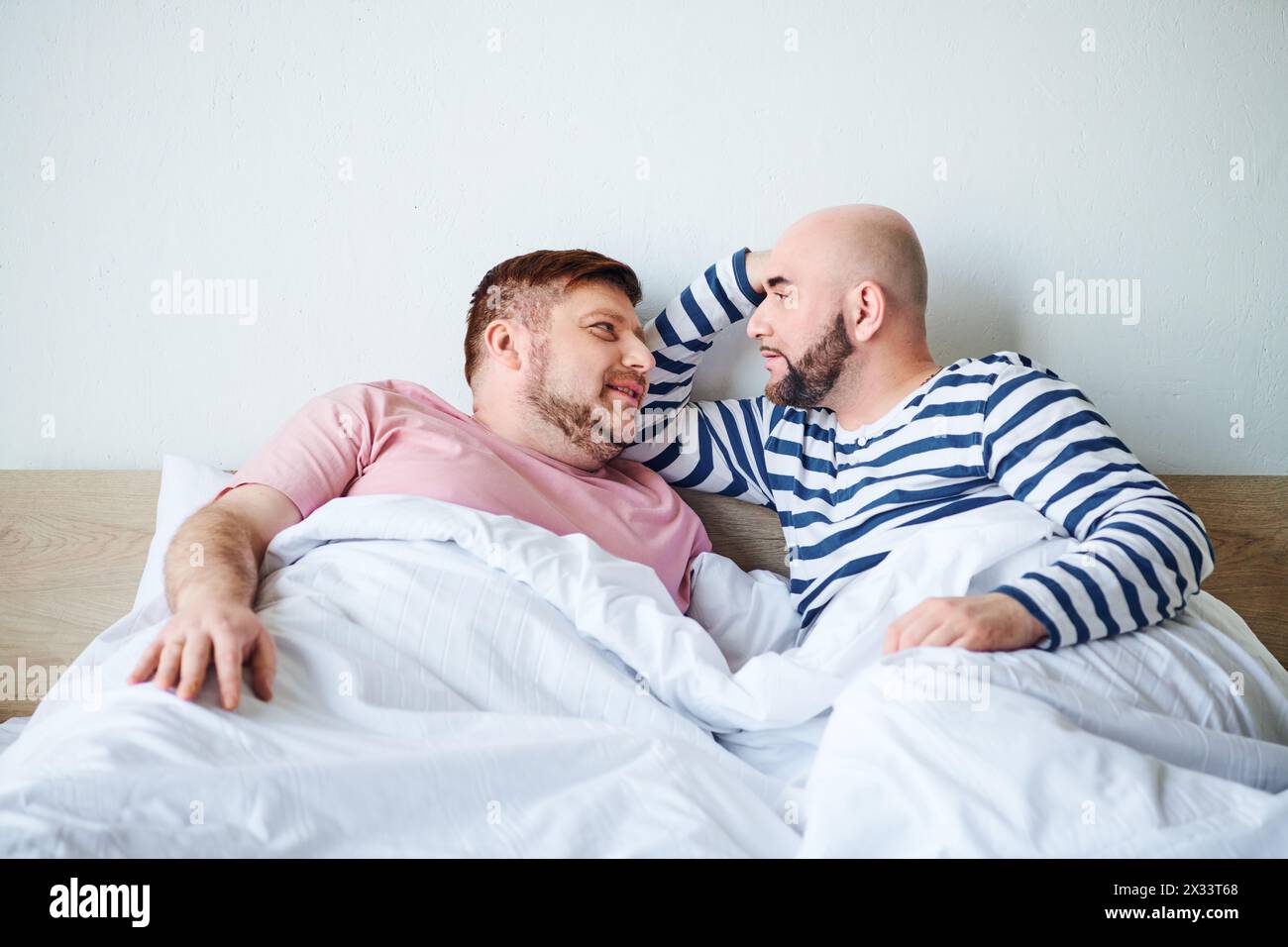 A pair of men laying side by side in bed, spending quality time together. Stock Photo