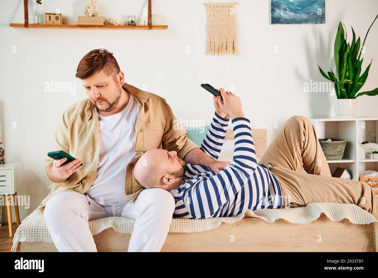A man sits on a bed next to his boyfriend. Stock Photo