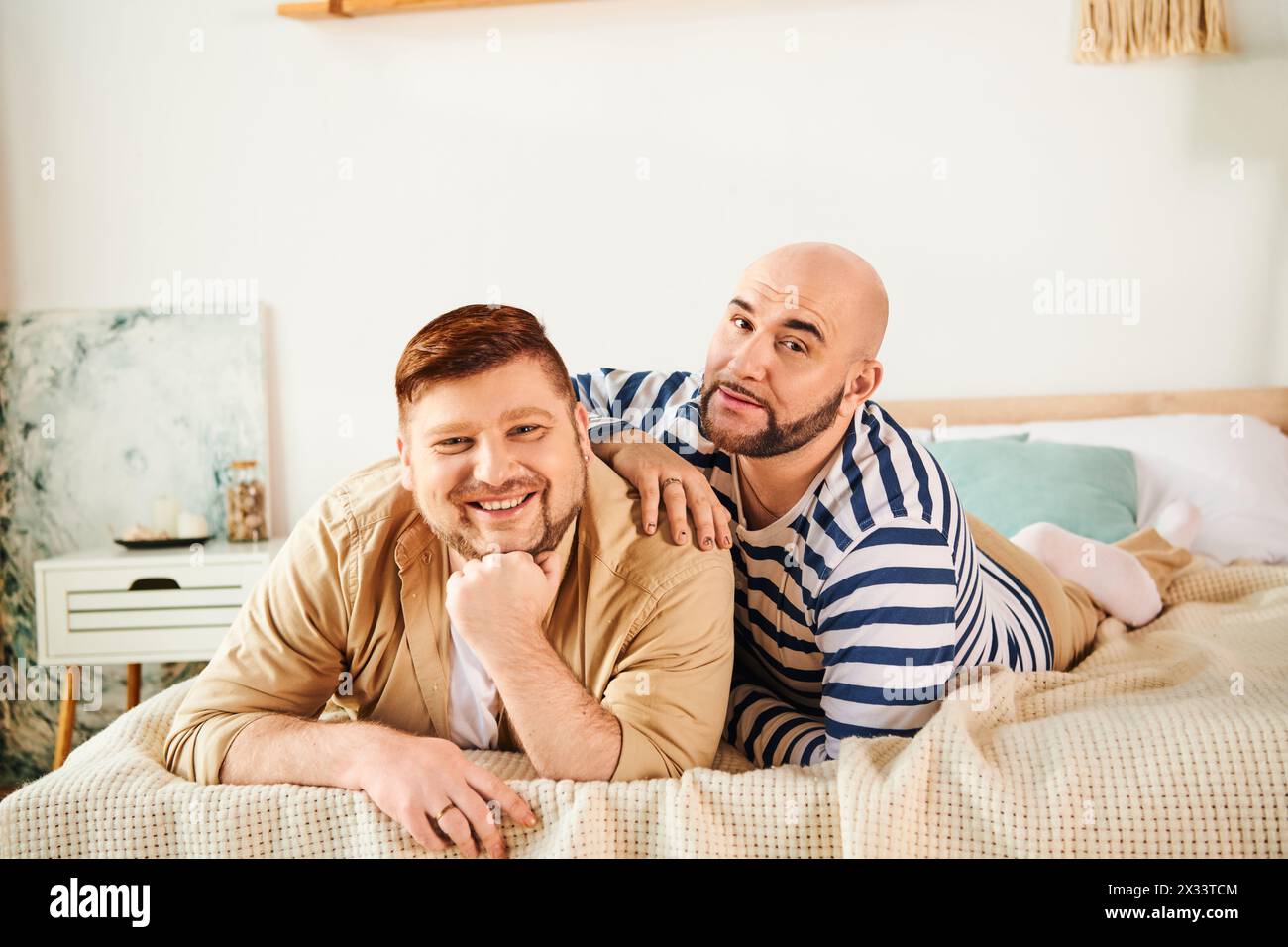 A couple of men enjoy a peaceful moment lounging on top of a bed. Stock Photo