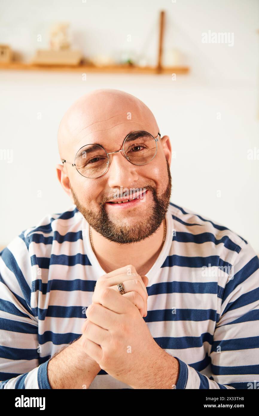 A bald man in glasses strikes a thoughtful pose at home. Stock Photo
