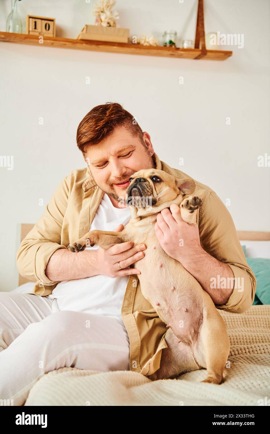 A man sitting on a bed, affectionately holding a small dog. Stock Photo