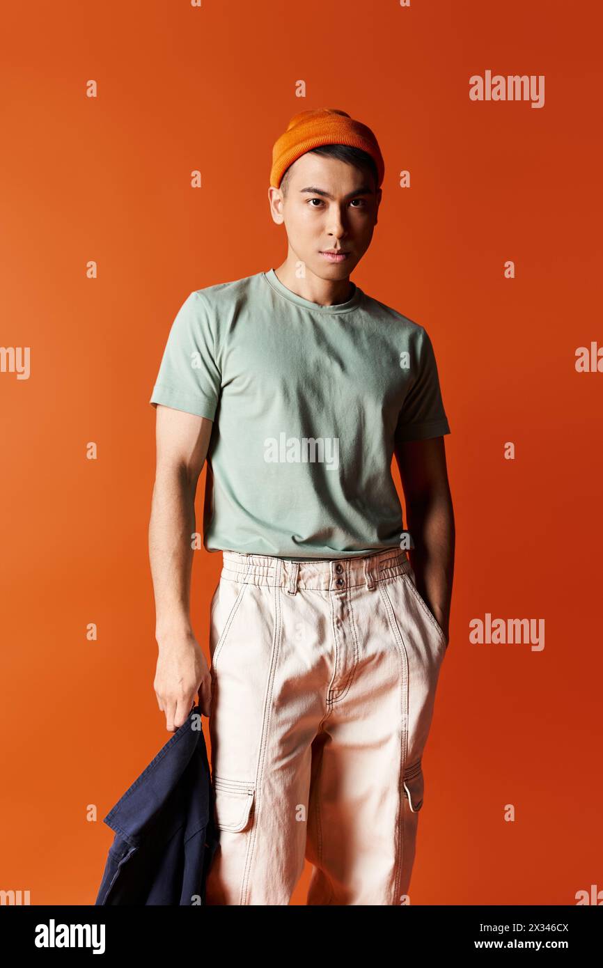 Handsome Asian man in a turban stands confidently in front of a vivid orange background in a studio setting. Stock Photo