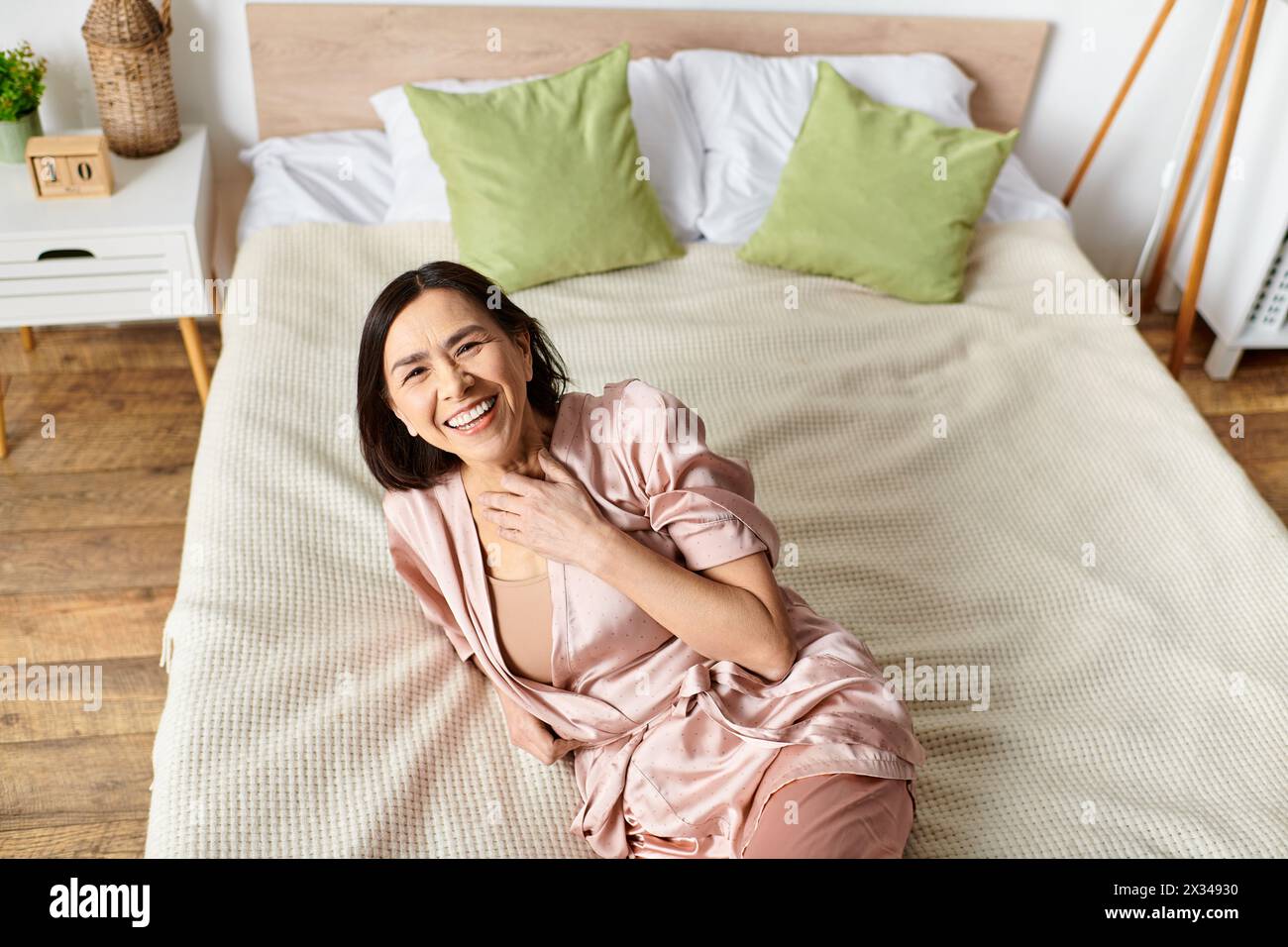 Mature woman relaxes on pink bed in cozy robe. Stock Photo