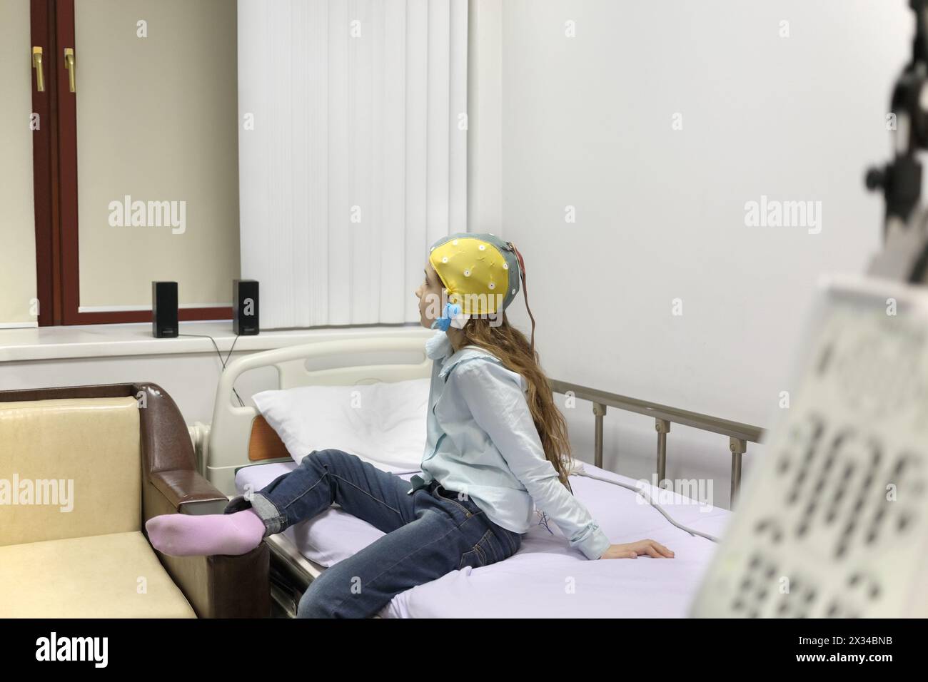 patient girl on procedure of removing of electroencephalogram, sitting on bed looking out window closed Stock Photo