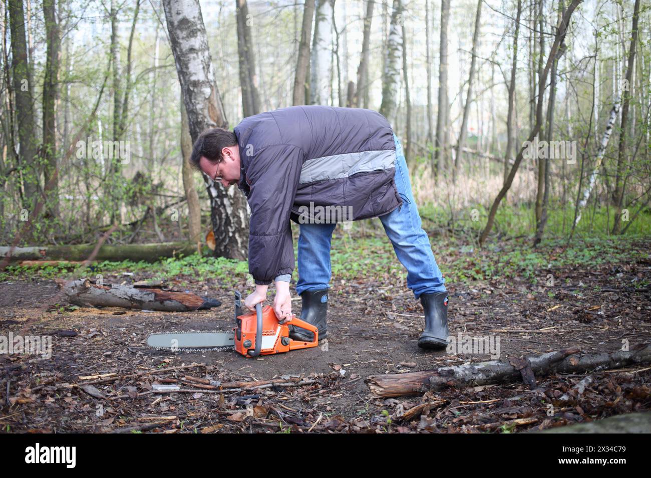 A man with glasses starts a chainsaw in the forest Stock Photo - Alamy