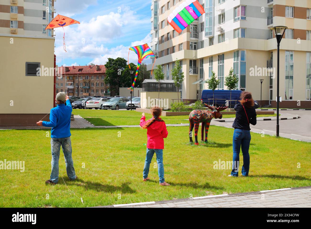 Mother with children launch kites on ground near house summer day Stock Photo