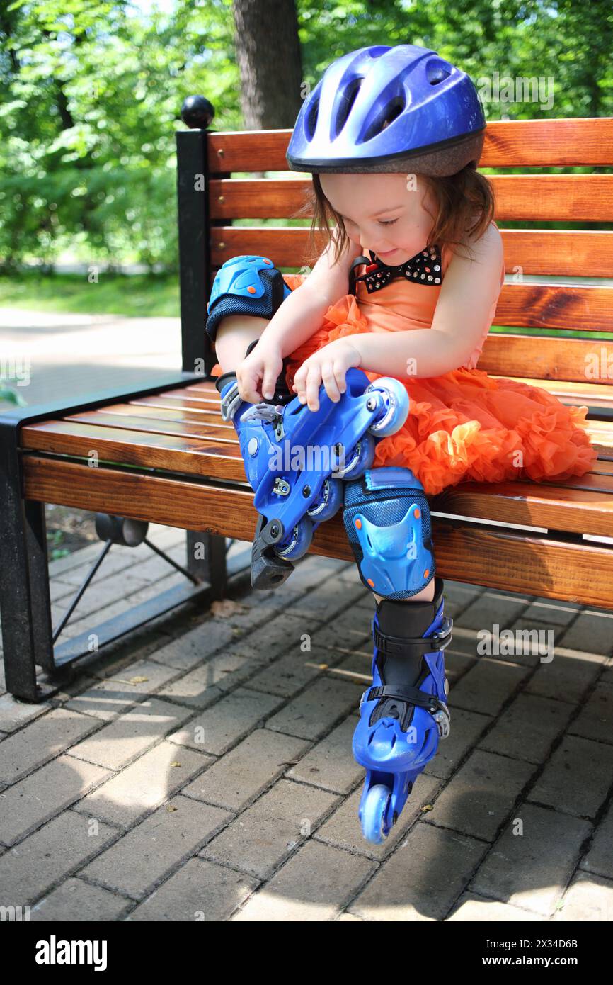 Little girl sitting on bench and removing roller skates at summer day Stock Photo