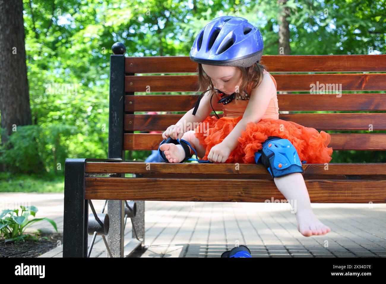 Little girl sits on bench and removes protective pads for roller skating Stock Photo