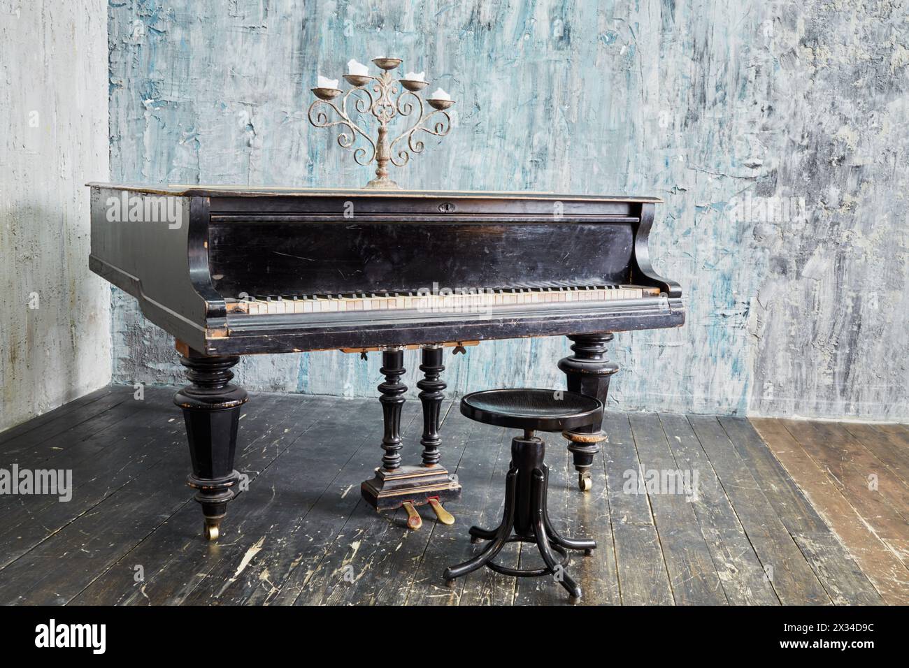 Old black grand piano stands in room with ragged walls and floor. Stock Photo